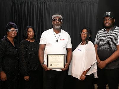 An honoree holds a framed certificate with members of the team.