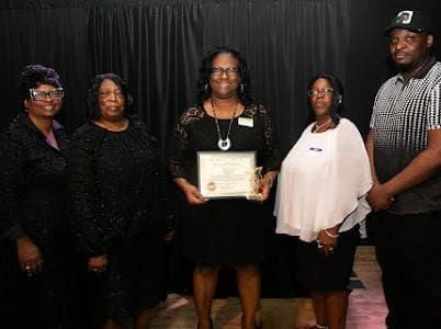 An honoree holds a certificate on stage with the team.