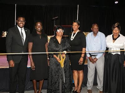 Leaders and guests stand behind a gold ribbon during a ribbon-cutting at the 20th anniversary celebration.