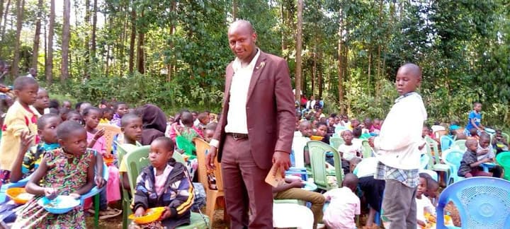 Bishop David Nyriki stands among dozens of children eating from bowls at an outdoor outreach meal.