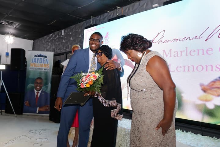 Evangelist Marlene G. Lemons is congratulated on stage beneath a screen displaying “Phenomenal Woman” and her name.