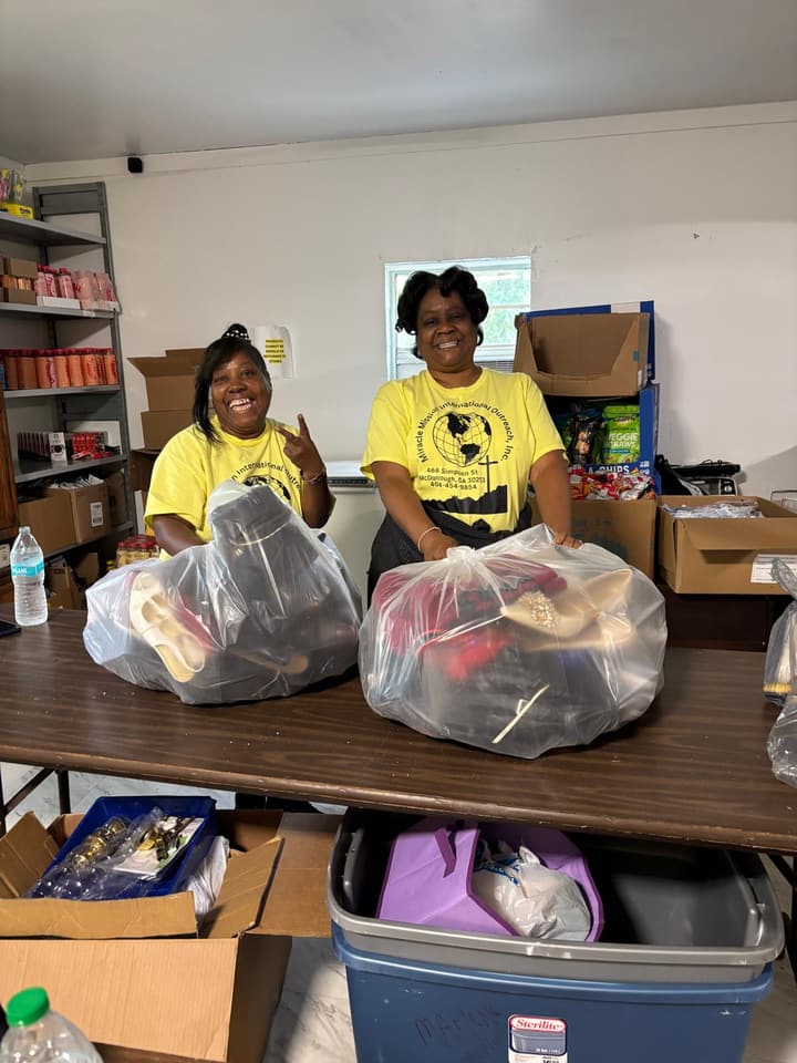 Two volunteers sort large bags of donated shoes and clothing.